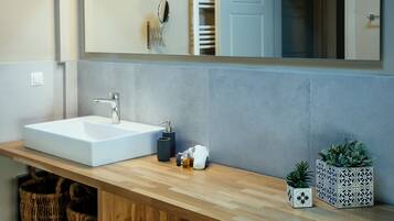 A modern bathroom with a large mirror, a white sink, and two potted plants.