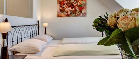 Una habitación de hotel con una cama, una mesita de noche, una lámpara y un florero con flores.