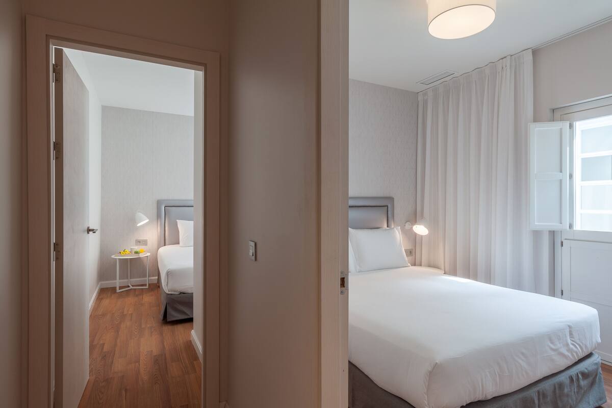 Quarto de hotel com cama, mesa de cabeceira, abajur e vista para o corredor.