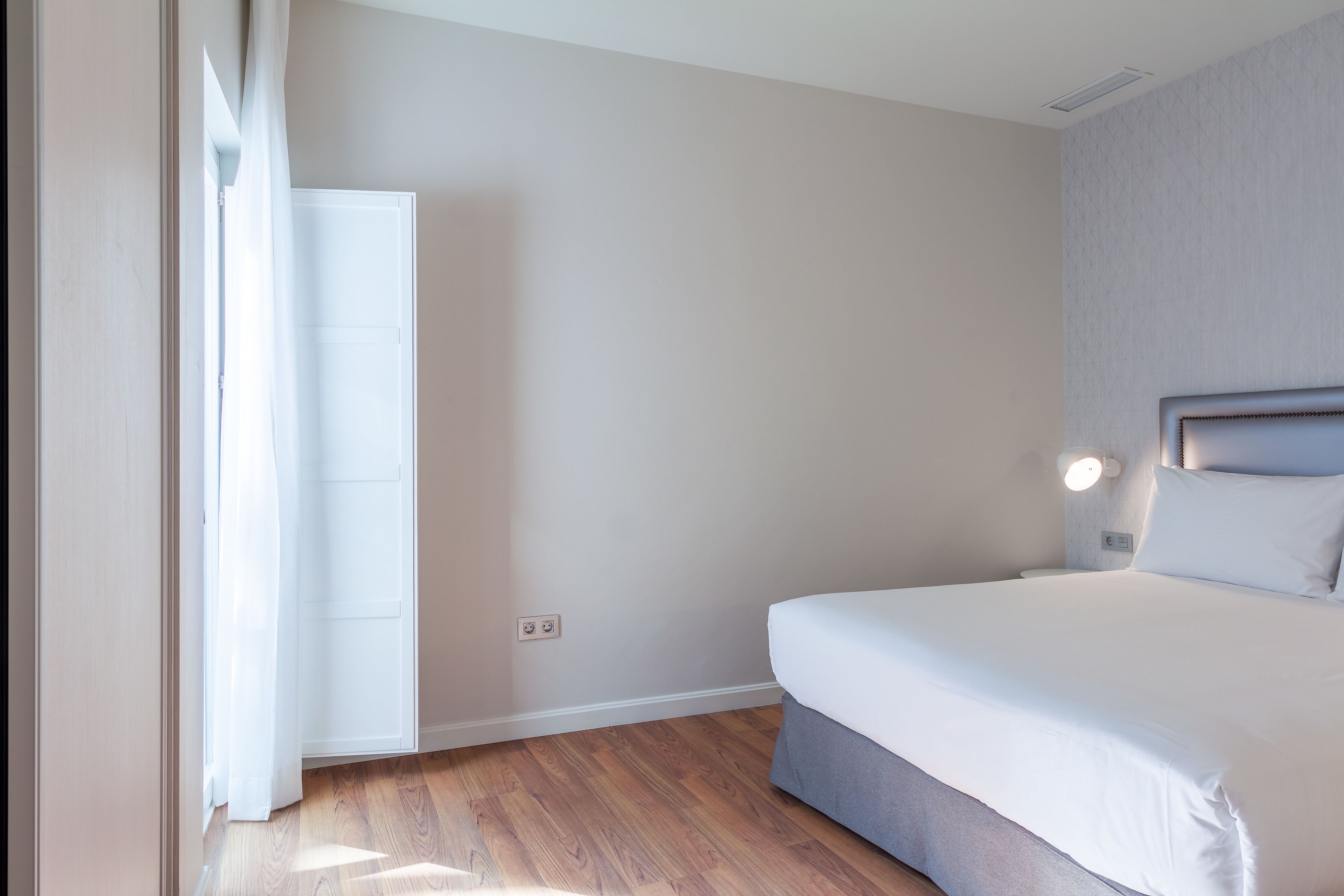 A bedroom with a bed, a nightstand, a wall-mounted light, and a door.