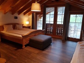 Un dormitorio de madera con una cama grande, un banco y un balcón con vistas al campo.