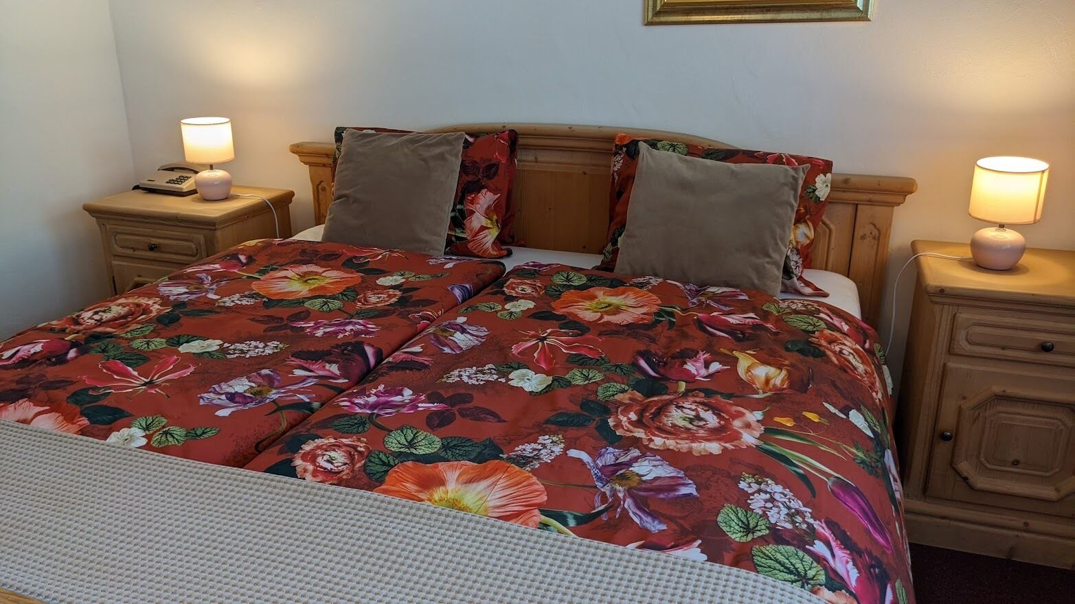 A bed with a floral bedspread, two pillows, and two bedside lamps on wooden nightstands.