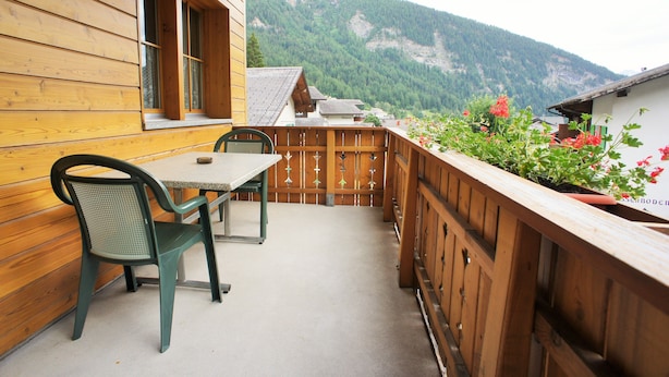 A wooden balcony with a table and chairs, overlooking a mountainous landscape.