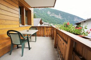 Un balcón de madera con una mesa y sillas, con vistas a un paisaje montañoso.