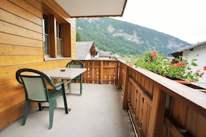 Un balcon en bois, agrémenté d’une table et de chaises, qui offre une vue sur un paysage montagneux.