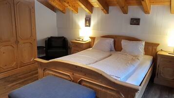 A wooden bed with a headboard, a bedside table, a lamp, and a wardrobe in a room with wooden beams on the ceiling.