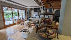 A dining area with a buffet setup, a television, and a view of the outdoors through large windows.