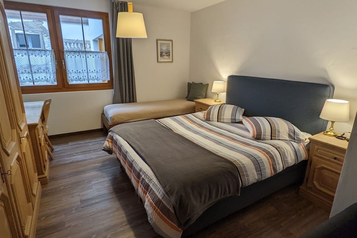 A bedroom with a bed, bedside tables, a window, and a view of the outside.