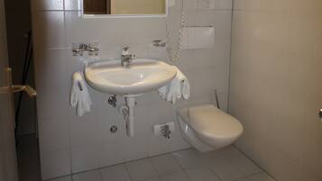 Un baño con lavamanos blanco, espejo, inodoro, vigas de madera en el techo y suelo de baldosas.