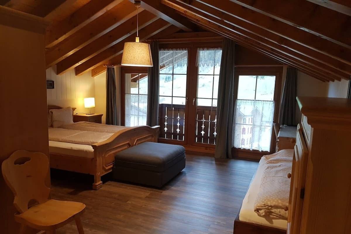 A cozy room with a bed, a chair, a desk, and a balcony with wooden railings.