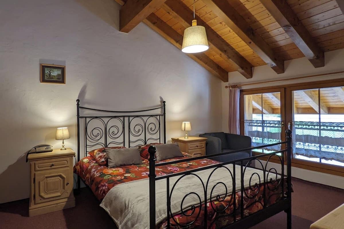 A bedroom with a bed, bedside tables, a lamp, a window with a view, and a ceiling with wooden beams.