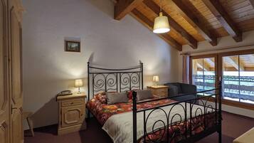 A bedroom with a bed, bedside tables, a lamp, a window with a view, and a ceiling with wooden beams.
