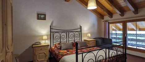 A bedroom with a bed, bedside tables, a lamp, a window with a view, and a ceiling with wooden beams.