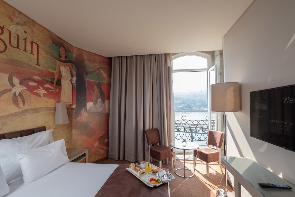 A hotel room with a bed, a tray with breakfast, a TV, a balcony with a view, and a mural on the wall.