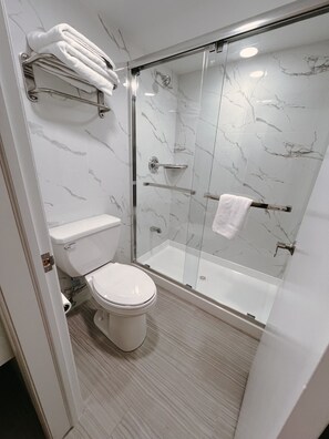 A modern bathroom with a glass-enclosed shower, a toilet, and a towel rack.