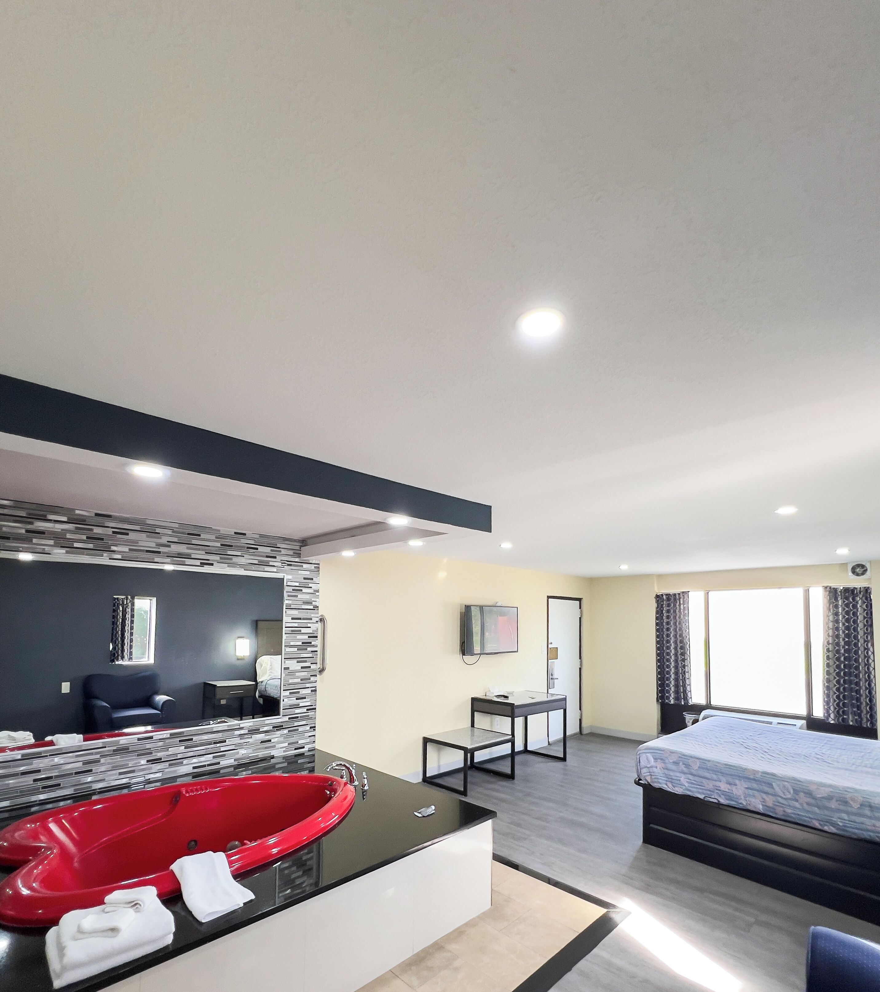 Une chambre d’hôtel moderne avec un grand lit, une baignoire rouge, un petit bureau et un téléviseur.