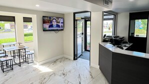 A modern reception area with a marble floor, a TV mounted on the wall, and a reception desk. - Travel Inn (New Castle)