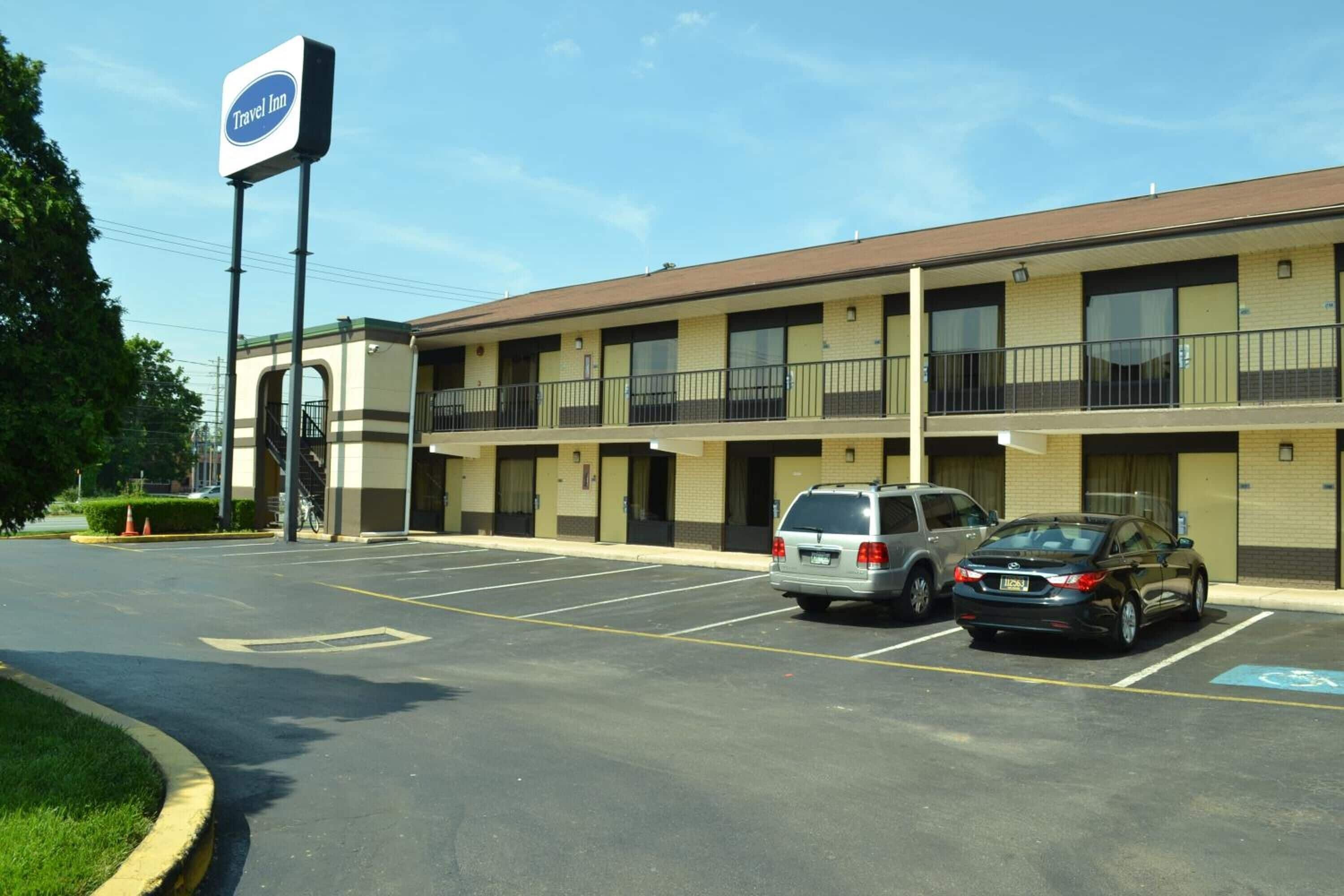 A Travel Inn with a two-story building, a parking lot with several cars, and a wheelchair-accessible parking space.