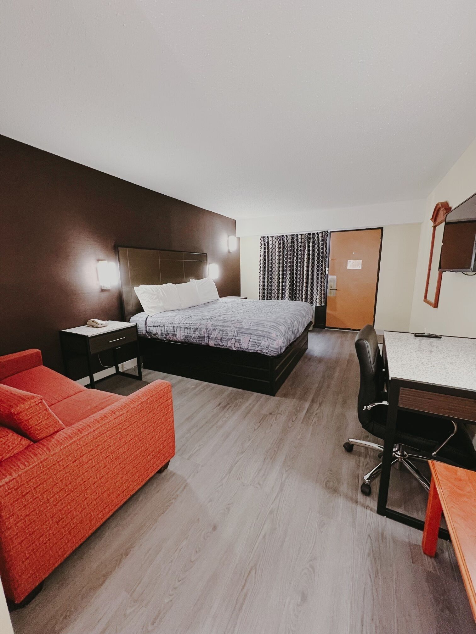Una habitación de hotel moderna con una cama grande, un escritorio, un sofá rojo y un espejo.