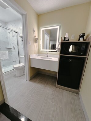 A modern bathroom with a glass shower enclosure, a white toilet, a sink with a mirror, and a microwave. - Travel Inn (New Castle)