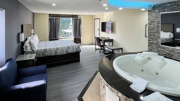 A modern hotel room with a bed, a desk, a chair, a large bathtub, and a TV. - Travel Inn (New Castle)