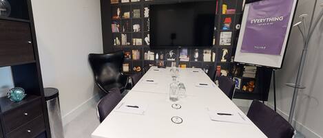 A conference room with a long white table, black chairs, a bookshelf with various items, and a screen displaying 'EVERYTHING'.