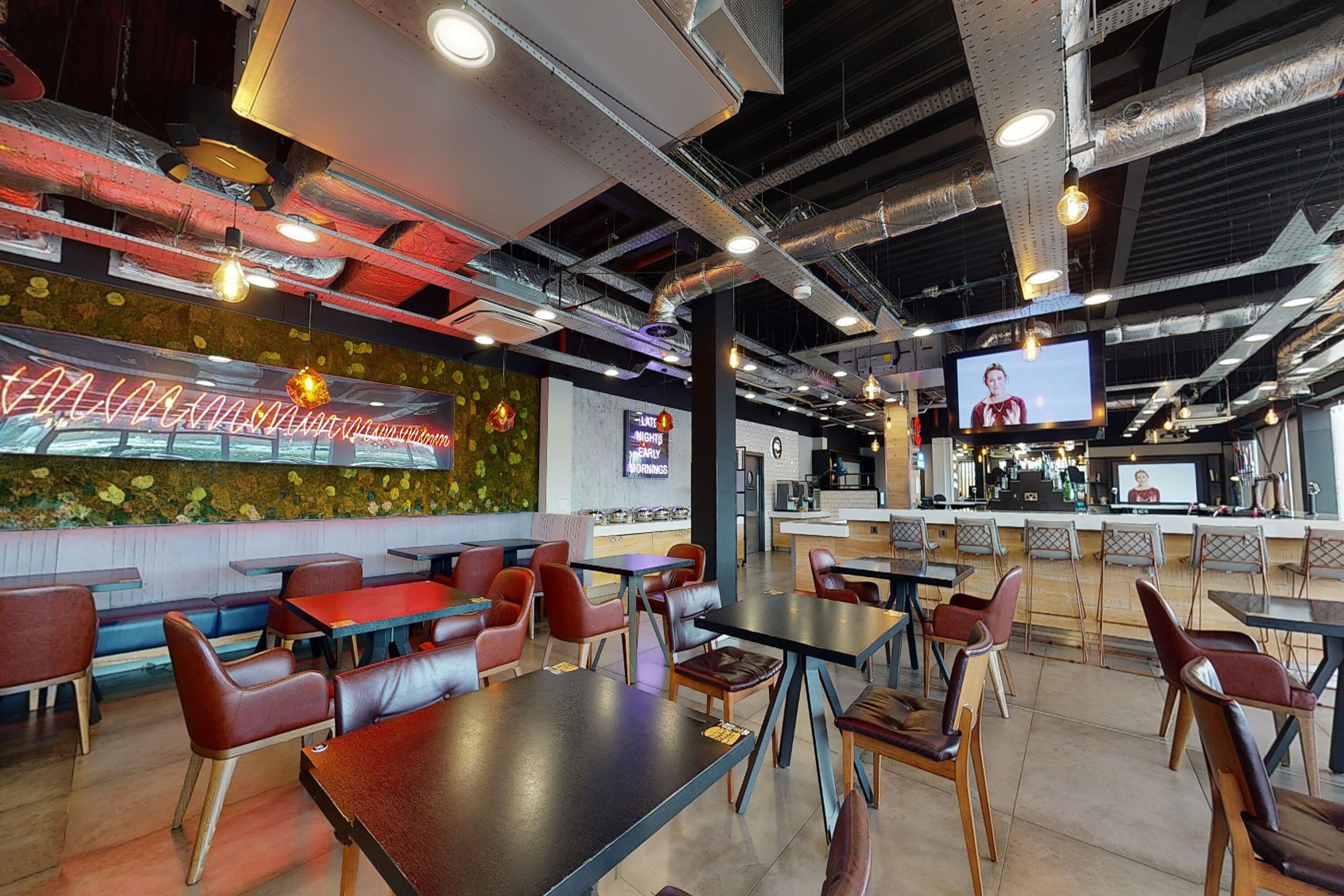Un interior de restaurante moderno con cabinas y mesas, una zona de bar y una pantalla de televisión.