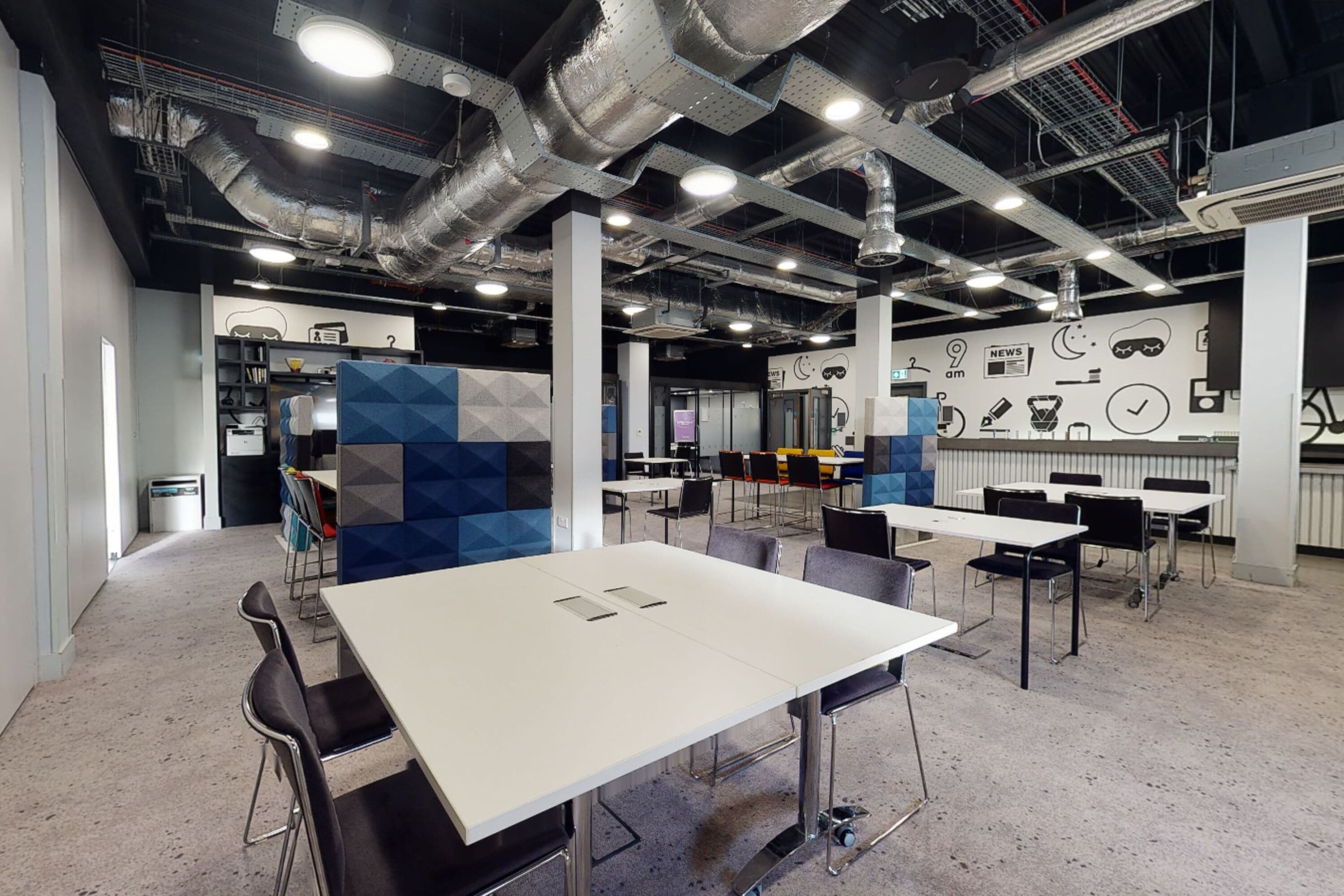 A modern conference room with white tables and black chairs, a visible air conditioning system, and a wall with various icons and a clock.
