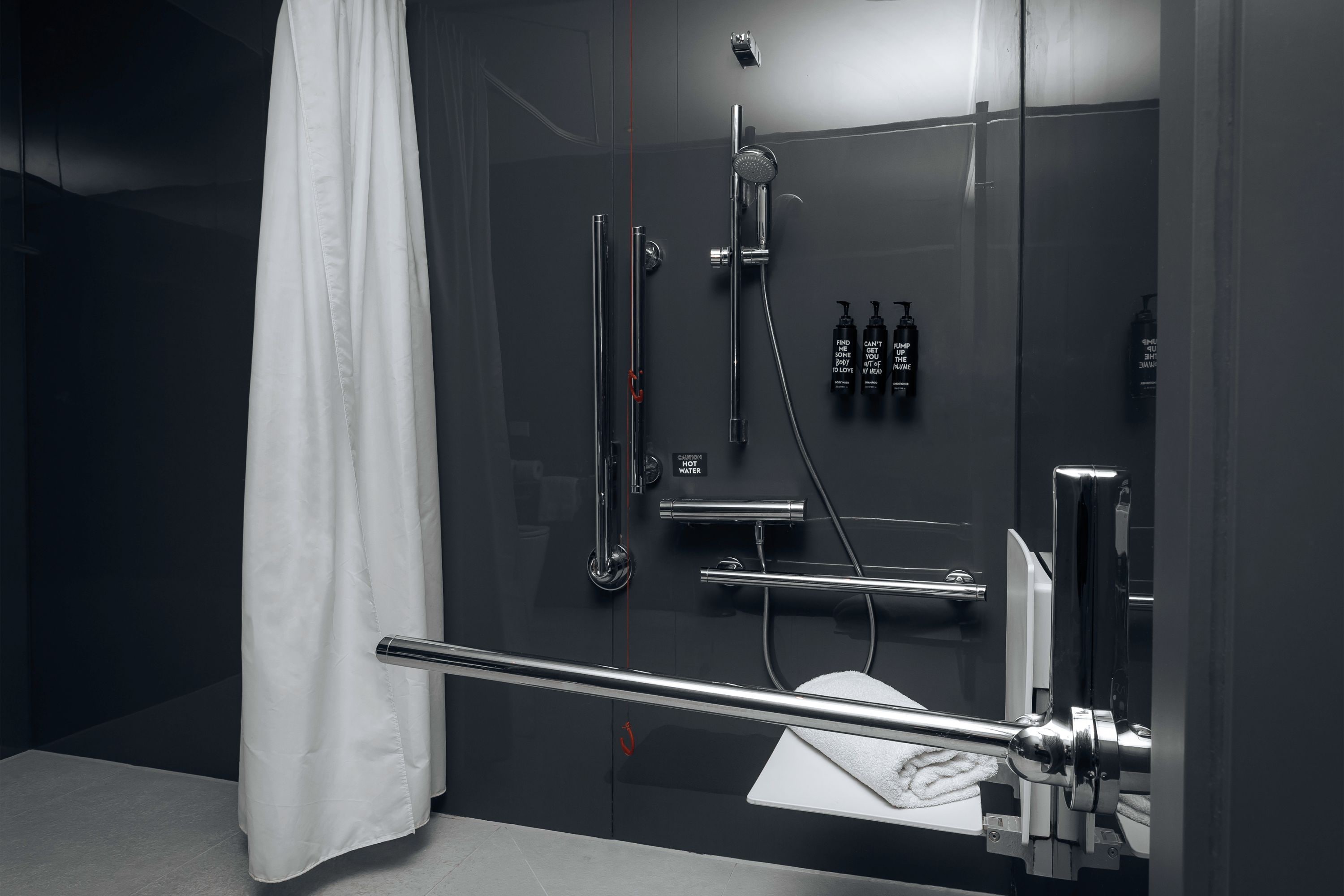 Une salle de bain moderne avec une douche à parois de verre, une serviette blanche et trois flacons de shampoing noirs.