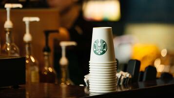 A stack of white Starbucks cups on a bar counter with a blurred background.