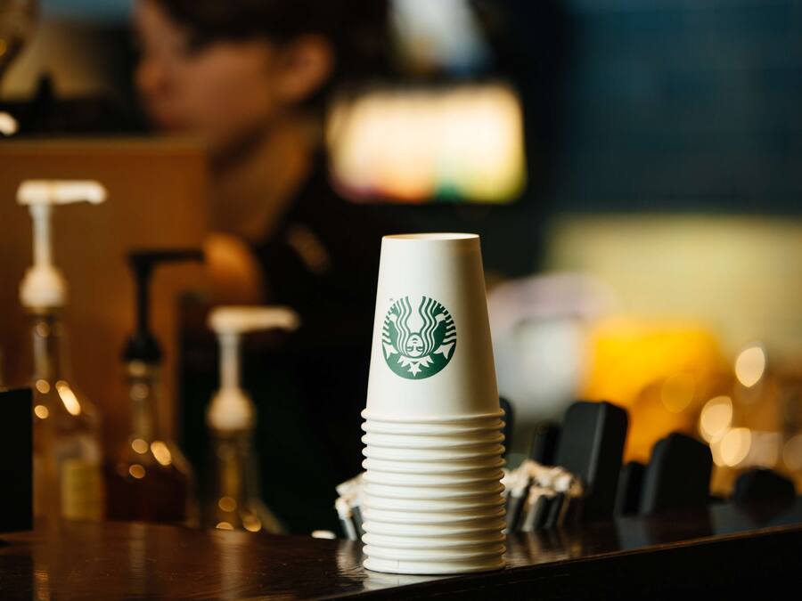 A stack of white Starbucks cups on a bar counter with a blurred background.