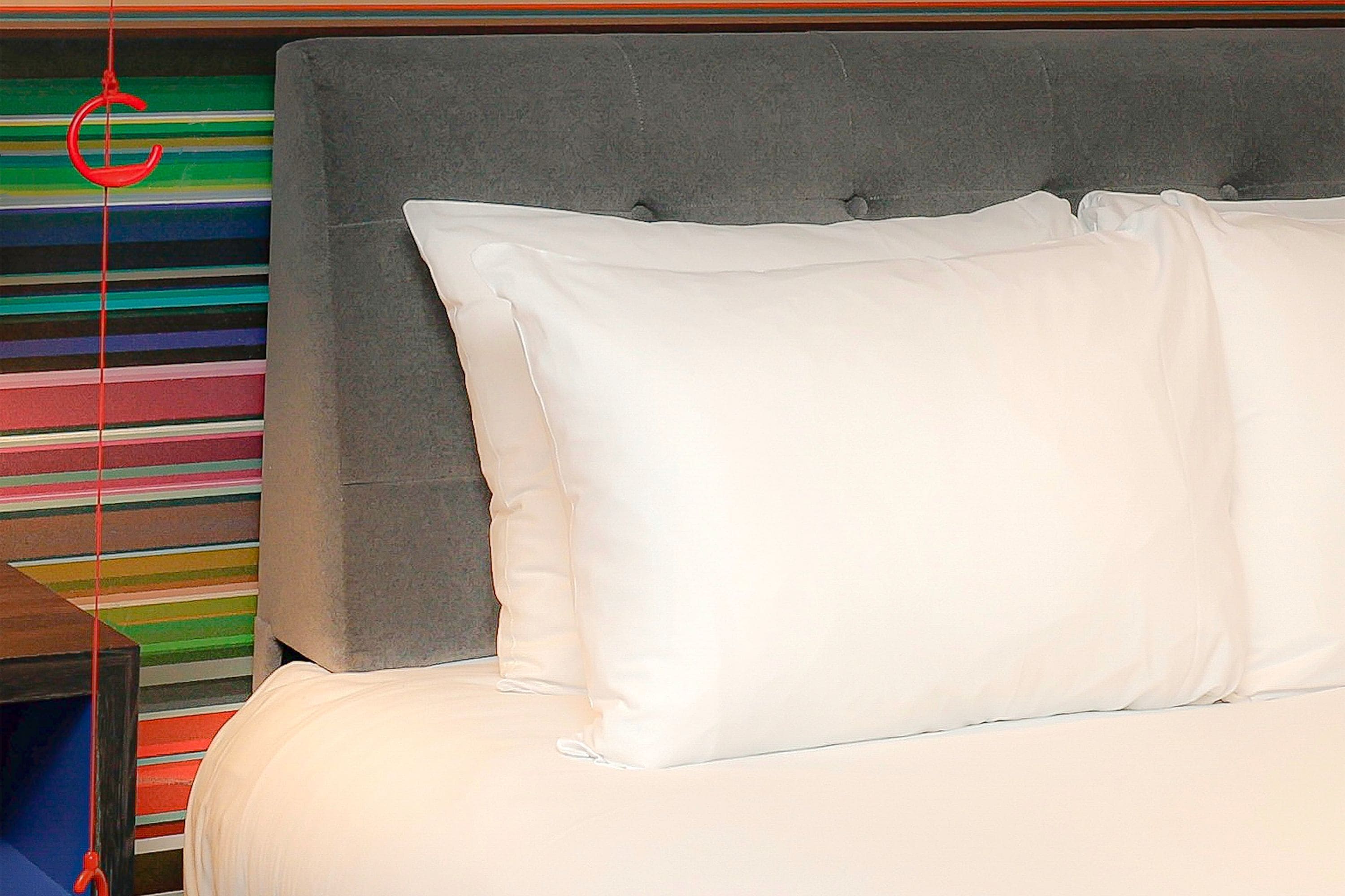 Una cama con ropa blanca y un cabecero gris en una habitación con paredes a rayas.