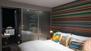Une chambre d’hôtel moderne avec un grand lit, une douche en verre et un mur rayé aux couleurs vives.