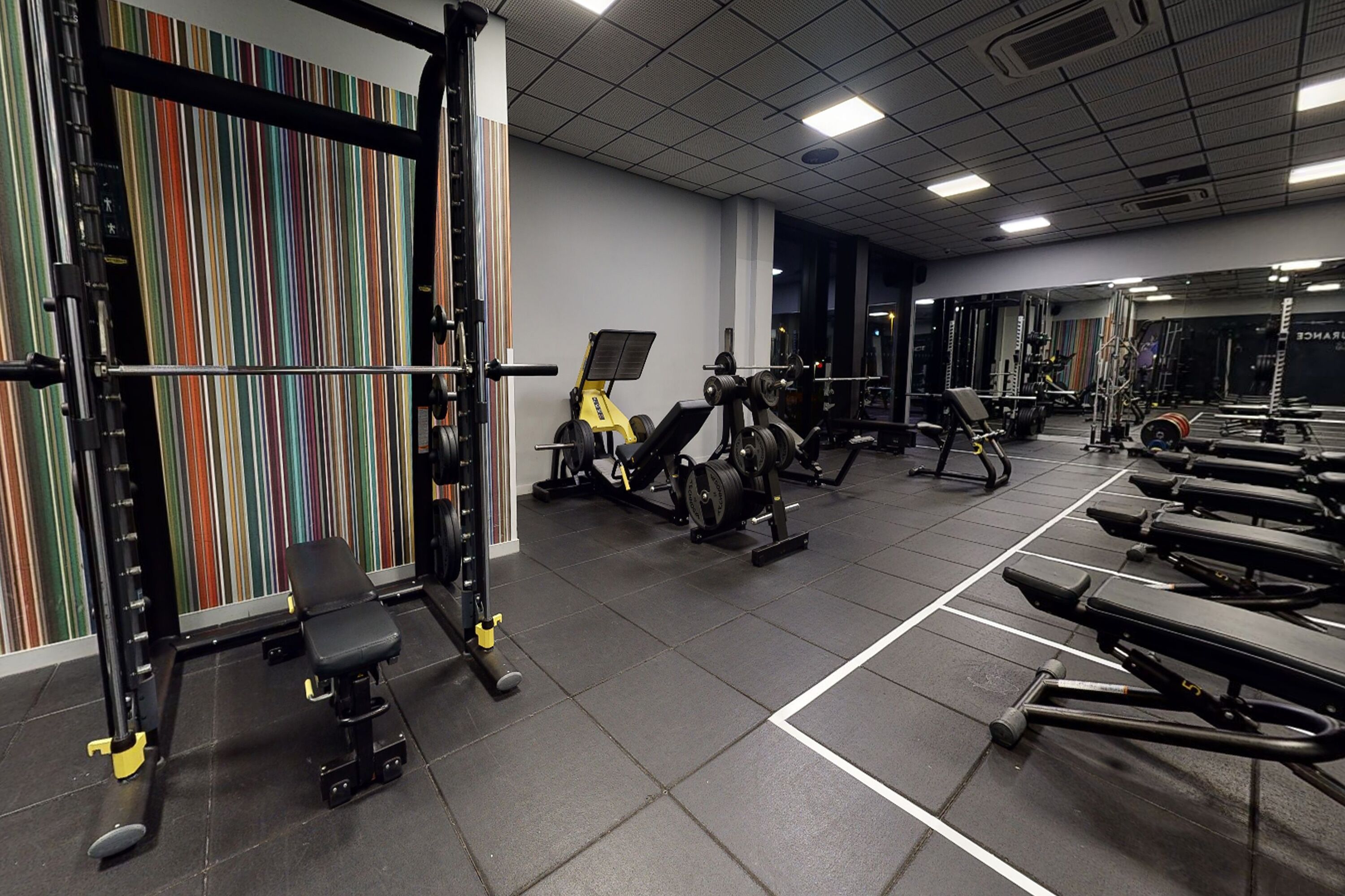 A gym with weightlifting equipment, benches, and a colorful striped wall.