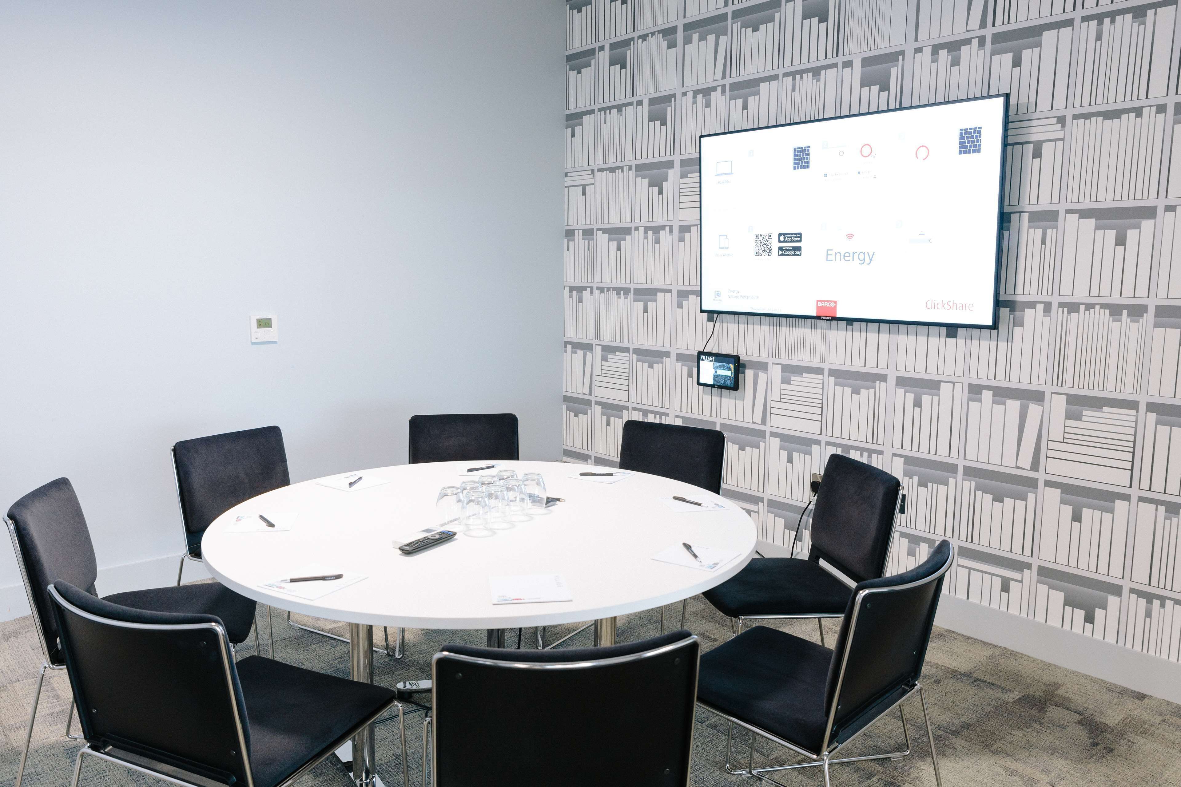 A conference room with a white table, black chairs, a screen displaying 'Energy' content, and a patterned wall.