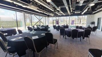 A conference room with multiple tables and chairs, large windows, and a visible clock on the wall.