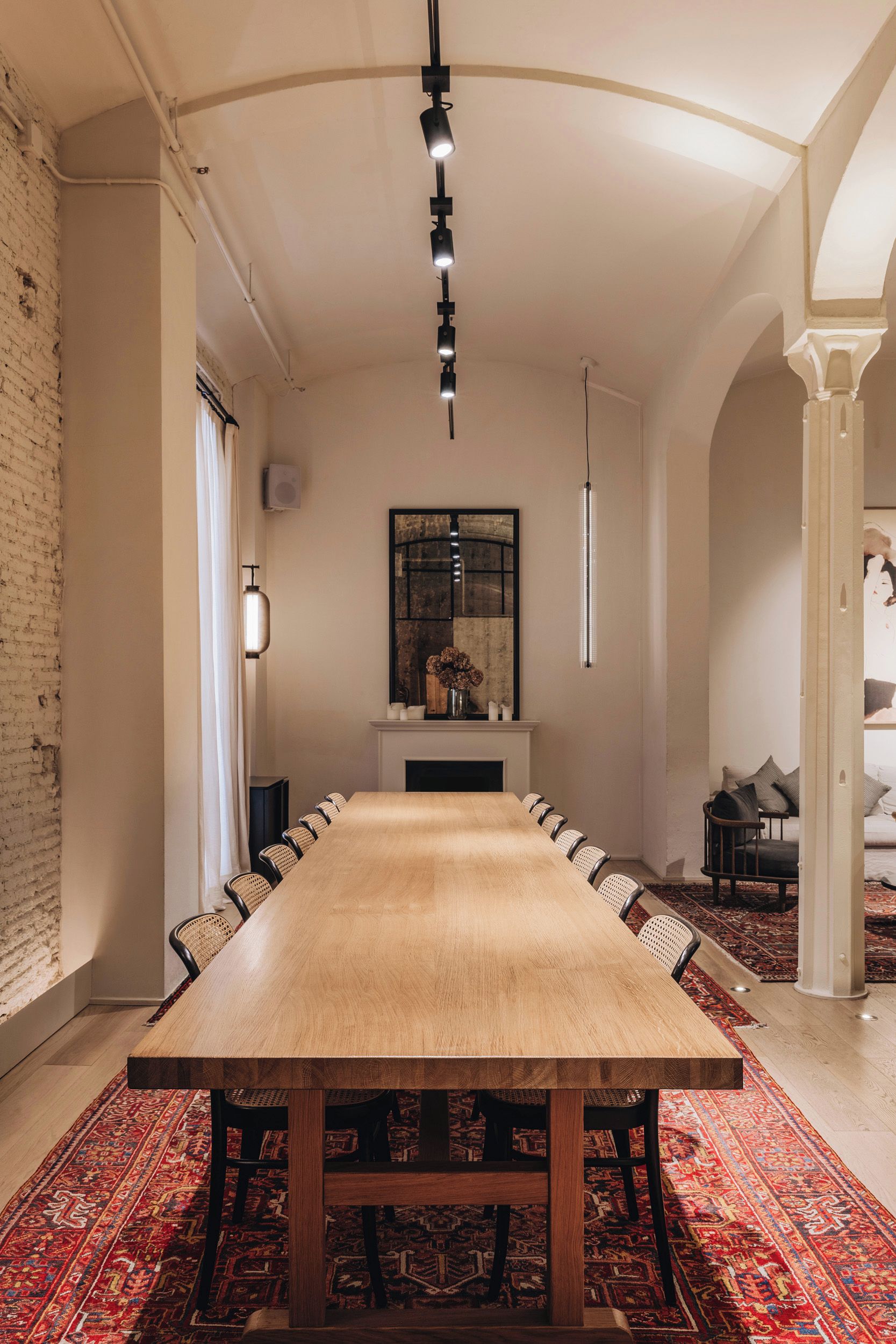 A long dining table with chairs, a fireplace, and a hanging light fixture in a room with brick walls and a patterned carpet.