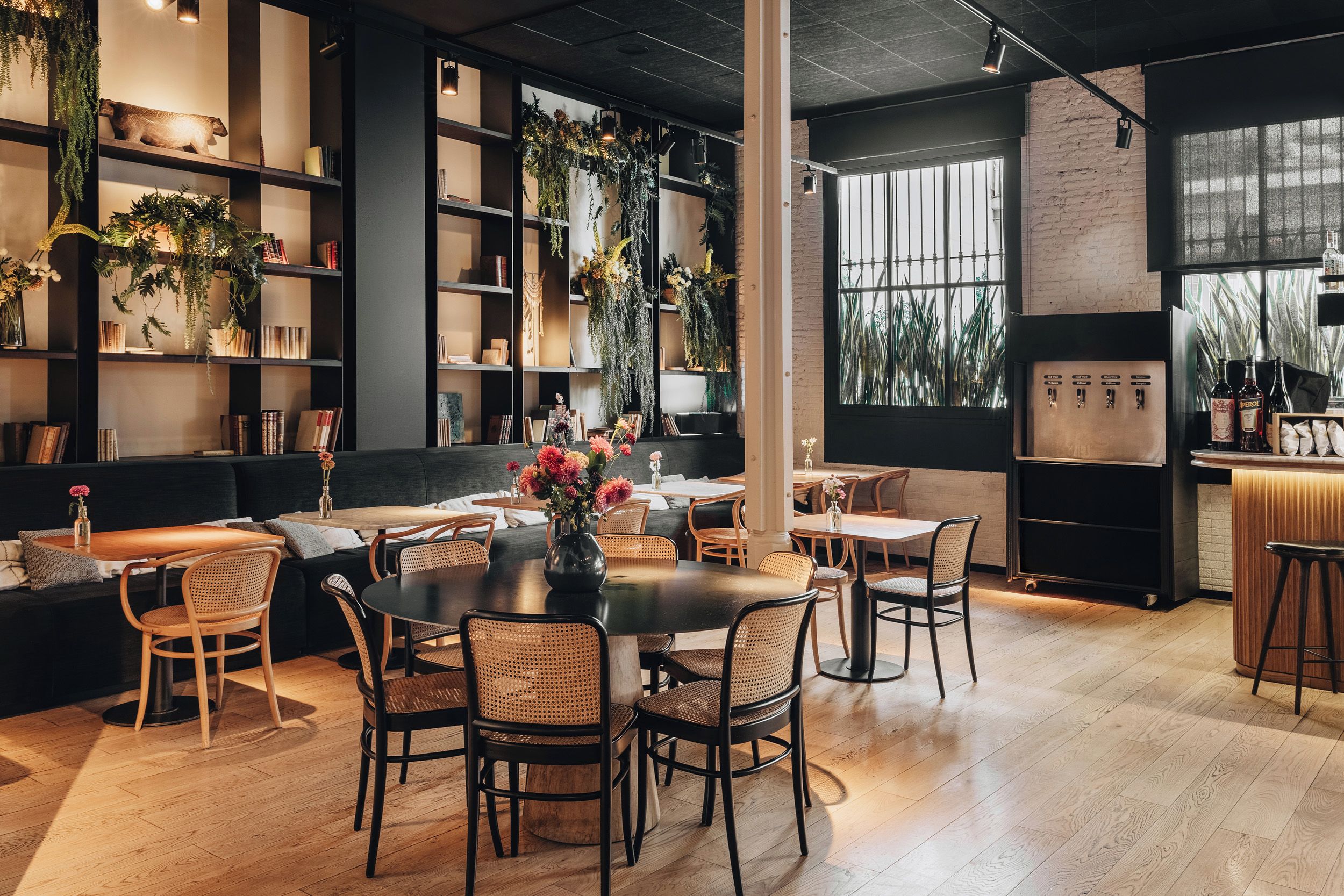 A modern interior with a bar area, seating arrangements, and a bookshelf with decorative plants.