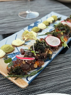 A long rectangular plate with various food items, including meat, greens, and radish slices, on a table with a woven placemat.