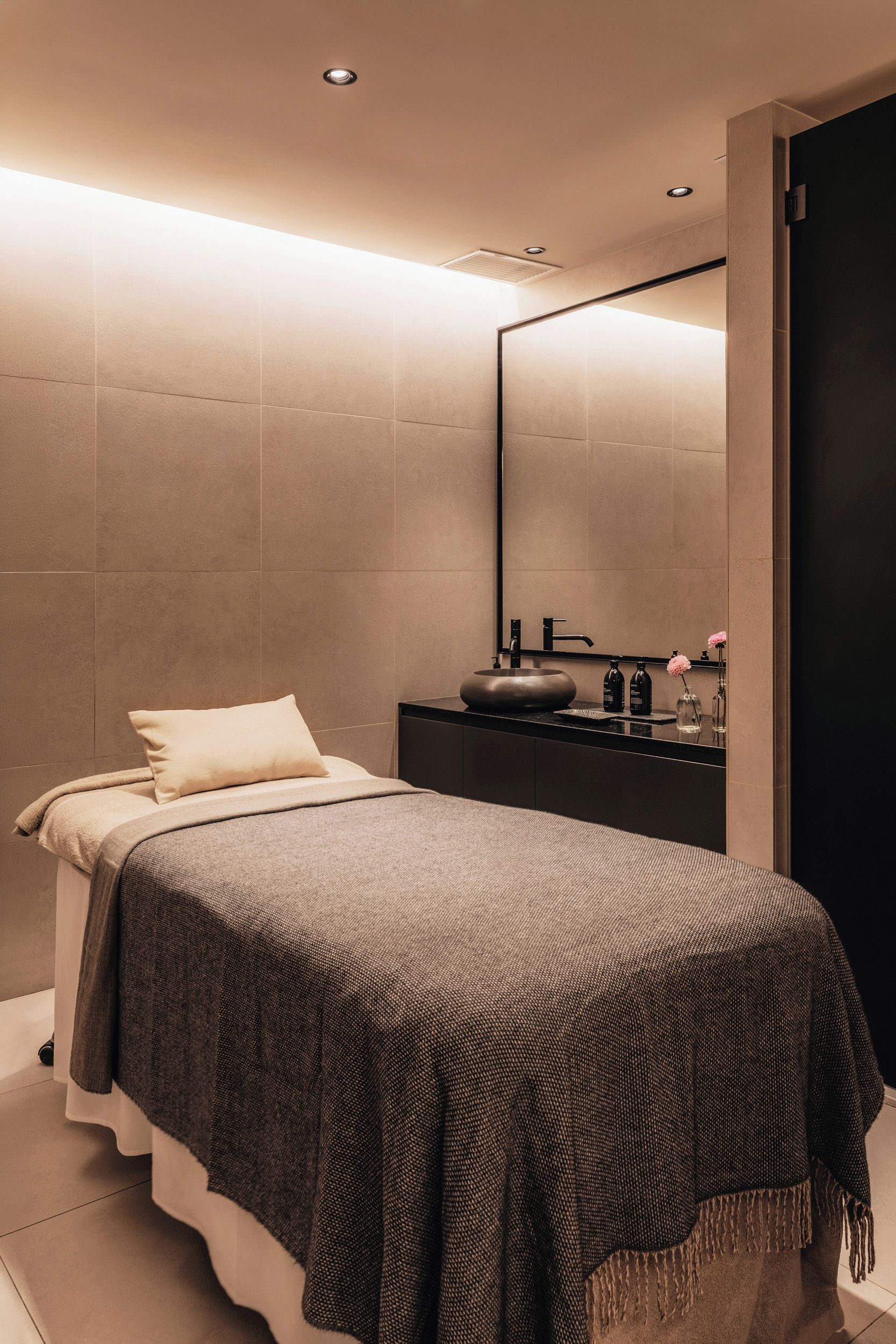 Un baño moderno con un espejo grande, un lavabo redondo y una cama con una manta texturizada.