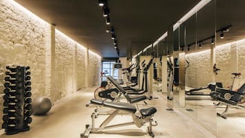 Un gimnasio con equipos de ejercicio variados, incluyendo cintas de correr y máquinas de pesas, y un espejo grande en la pared.