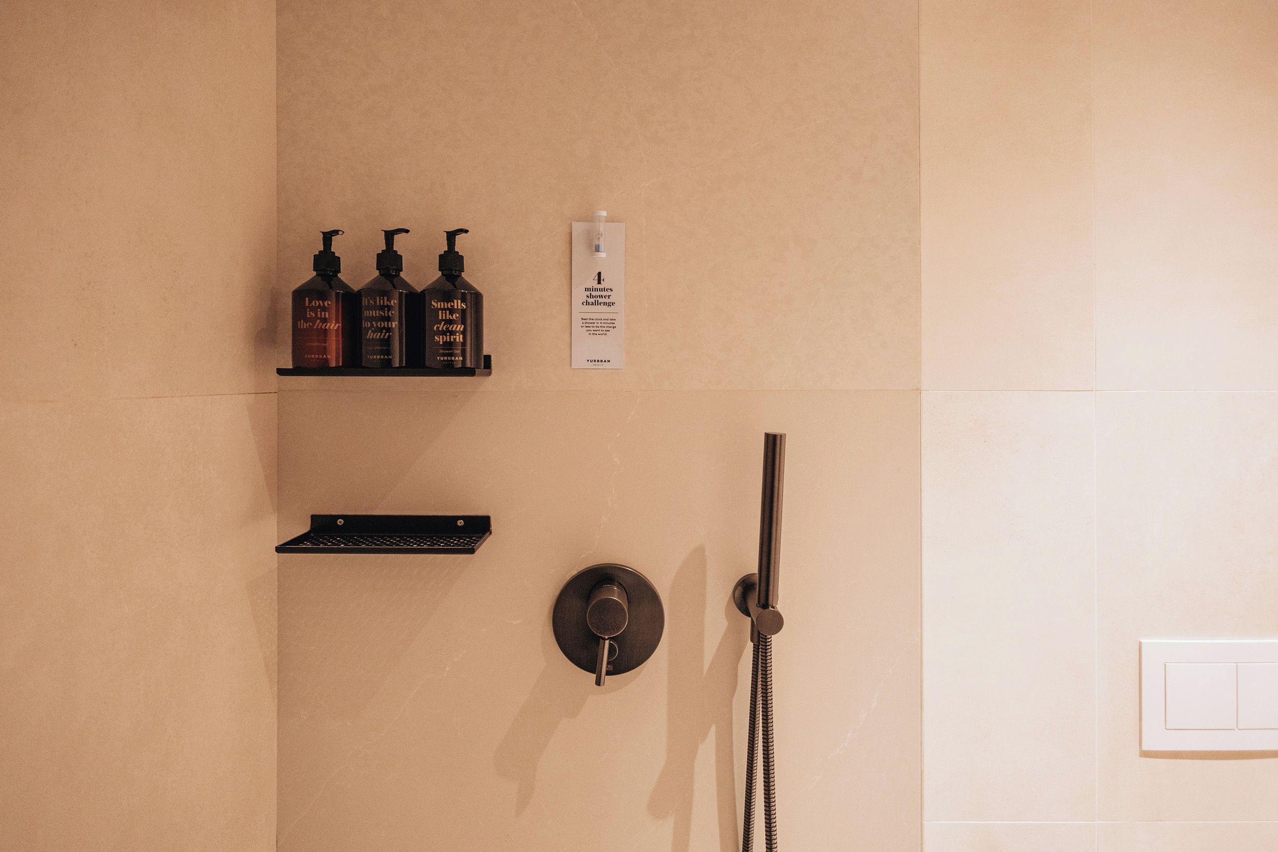 Un baño con ducha, toallero y tres botellas de champú en un estante.