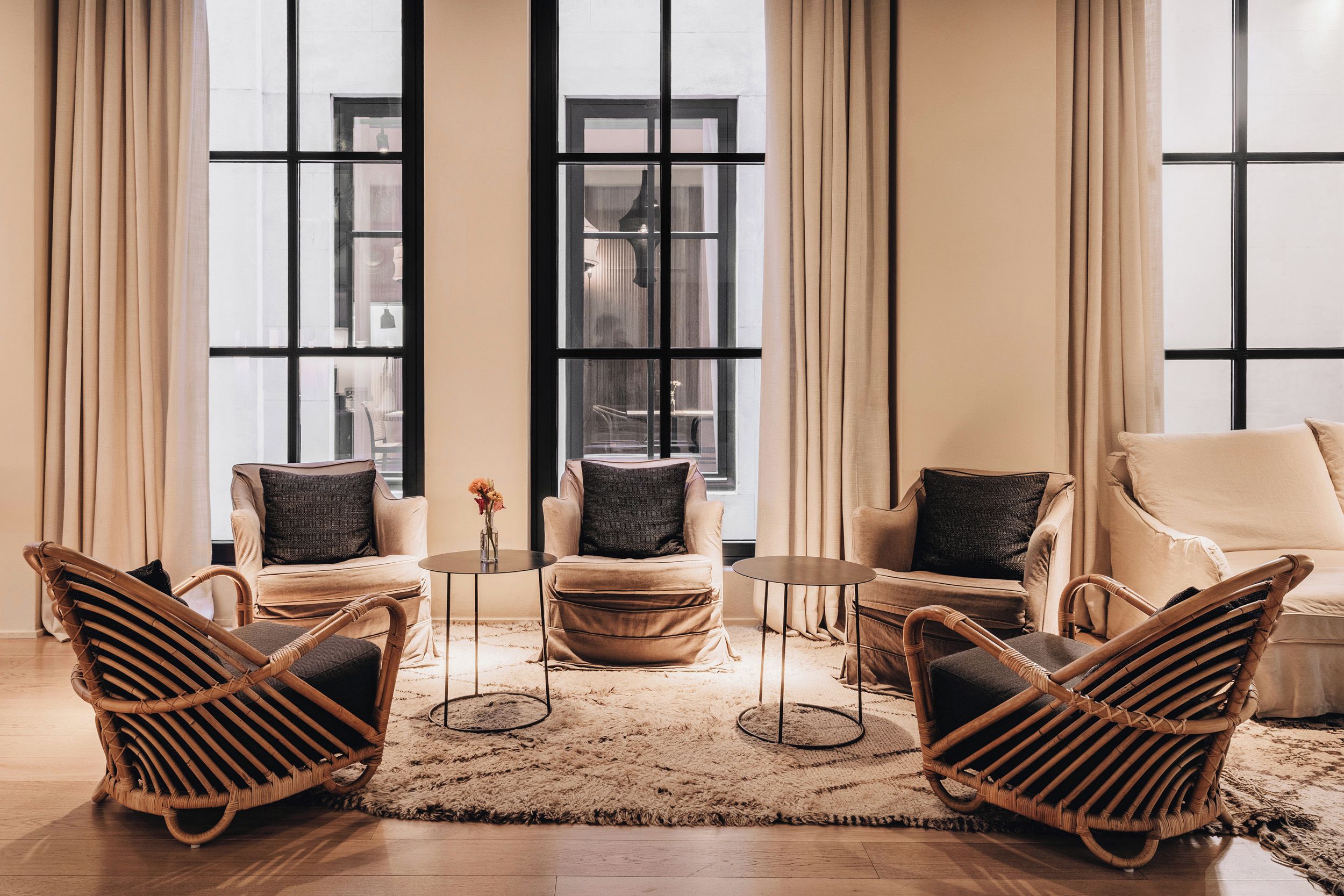 Een kamer met grote ramen, een zithoek, twee fauteuils, een kleine ronde tafel en een decoratieve vaas.