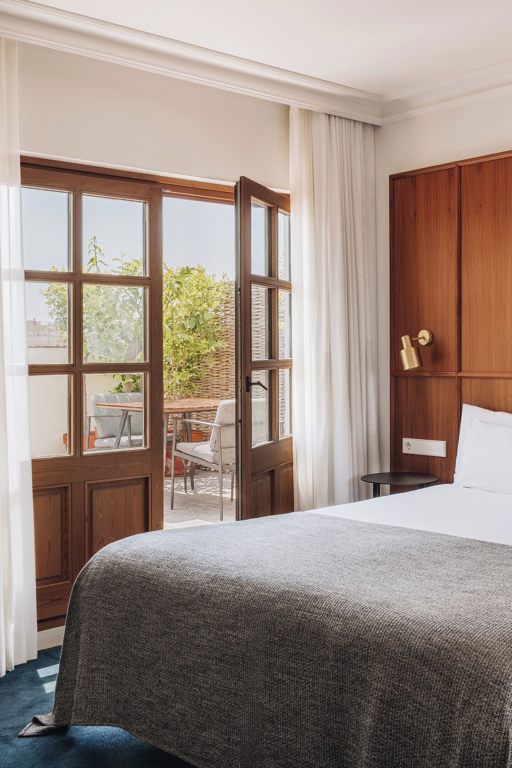 Ein Hotelzimmer mit einem großen Bett, einem Holzschrank, einem kleinen Tisch und Blick ins Freie durch eine Glastür.