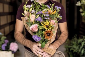 Eine Person hält einen Blumenstrauß mit dem Aufdruck 'TRAVELER FLOWERS 26 08010 Barcelona'.