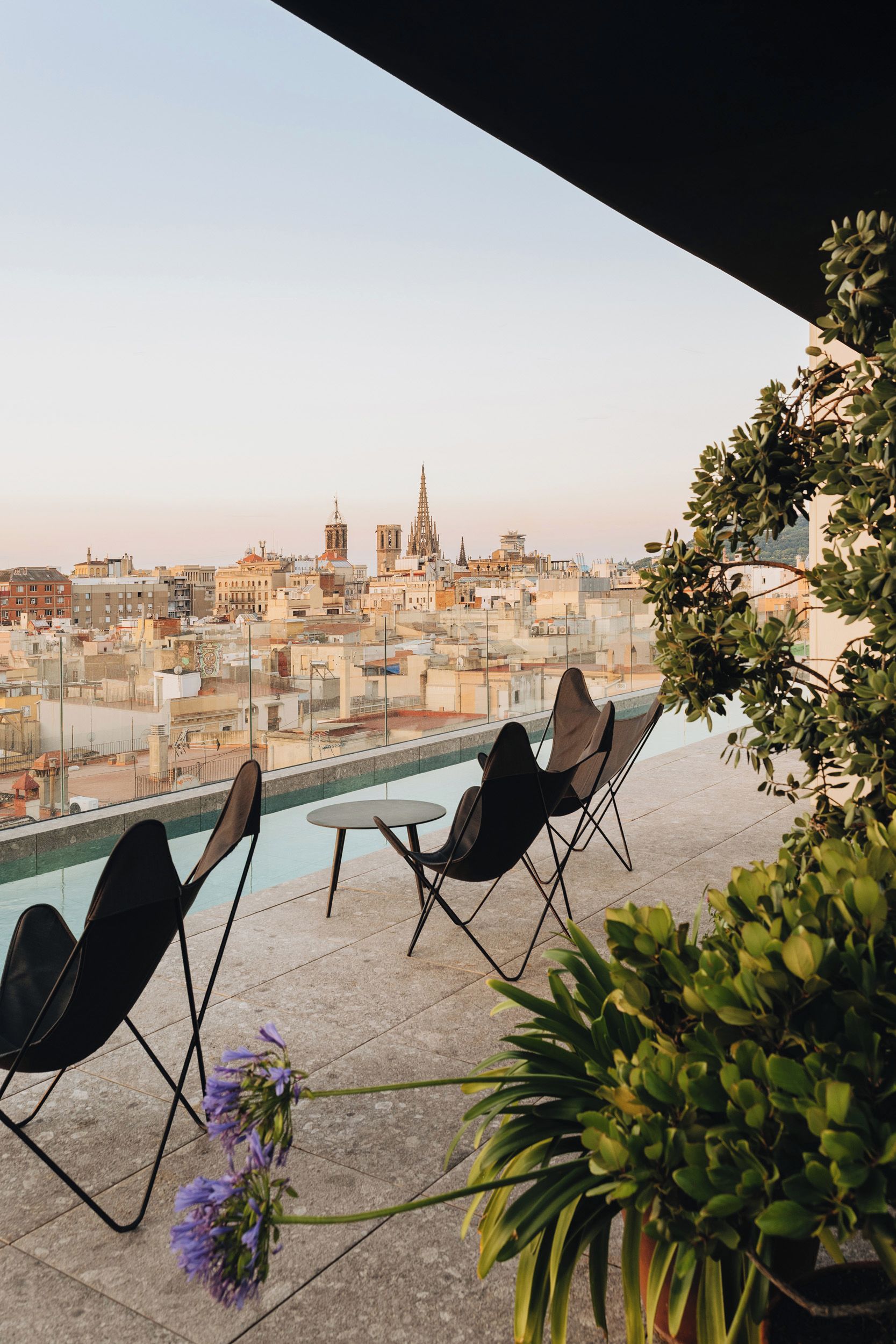 Una terraza en la azotea con piscina, sillas y vistas a un paisaje urbano que incluye una catedral.