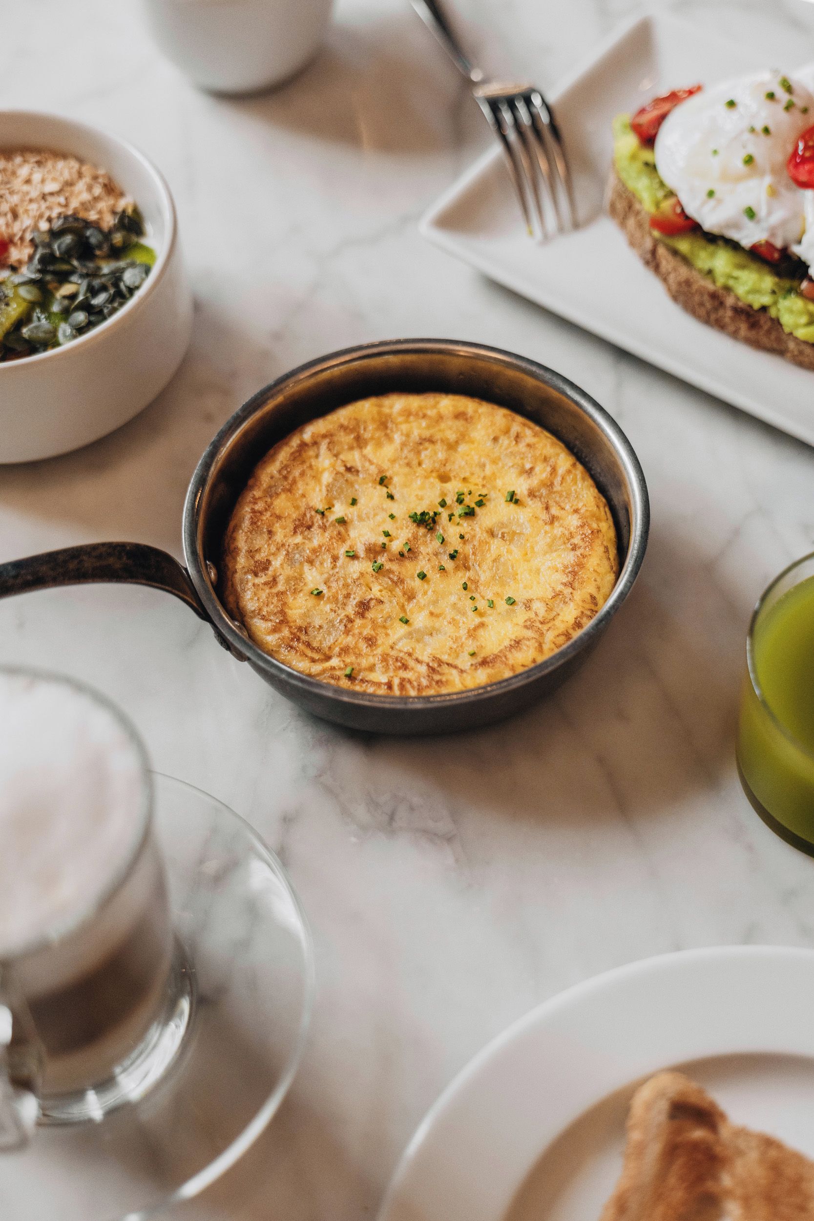 Een ontbijtsetting met een koekenpan vol eieren, een kop koffie en een bord met toast en avocado.