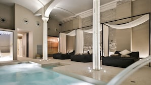 A modern indoor pool area with a jacuzzi, black sofas, and a large window with sheer curtains.