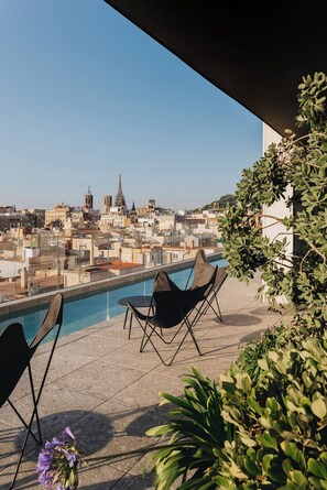 Eine Dachterrasse mit Pool, zwei Stühlen und Blick auf eine Stadtlandschaft mit historischen Gebäuden.