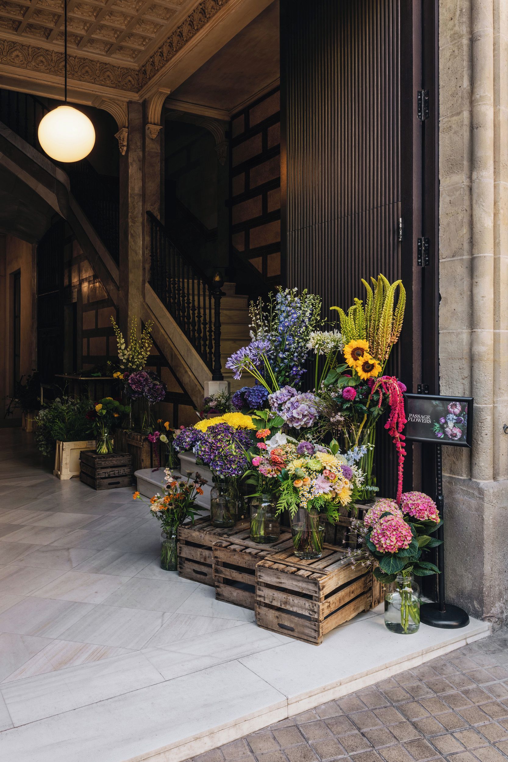 Un'arrangiazione floreale in una hall con una scalinata e un cartello che recita 'Passage Flowers'.